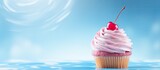 Copy space image of a solo cupcake adorned with swirls of pink icing and topped with a cherry against a blue backdrop