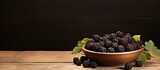 A wooden bowl filled with fresh blackberries is placed on a wooden table with a paper card creating a picturesque copy space image