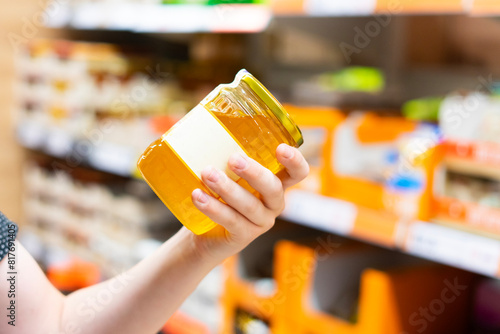 Young male hand holds honey on a blurred background, a row of shelves with groceries in supermarket