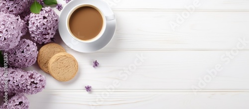 Morning concept with a bouquet of lilacs a cup of coffee and sandwich biscuits on a white wooden background creating a copy space image