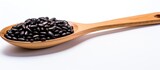 A copy space image of wooden spoon resting on white background amidst black beans