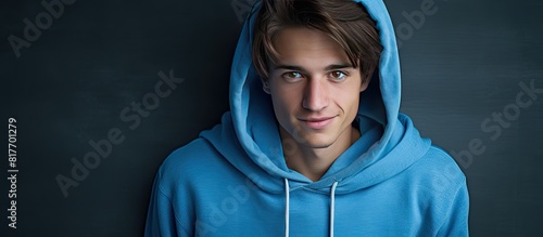 A jovial American young adult wearing a blue hoodie and jeans poses in a portrait against a simple background creating a copy space image