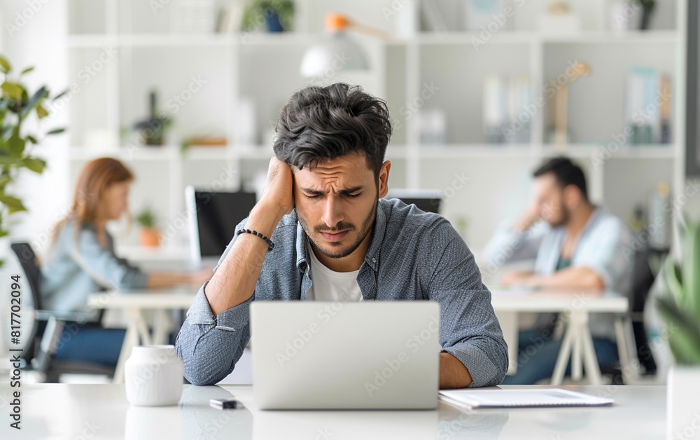 Young office worker sitting at a desk in a office with laptop on the table, stressing over work. Young office worker sitting at a desk in a office with laptop on the table, stressing over work.