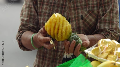 A Vietnamese street vendor delicately slicing a ripe yellow pineapple with a knife, using his bicycle as mobile fruit stall to bring the flavors of tropical fruit to locals and tourists at Hanoi