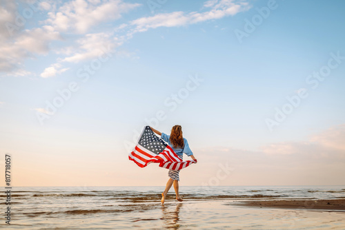 Obraz na plátně Young woman holding national American flag cover ocean beach holiday travel at summer romantic sunset