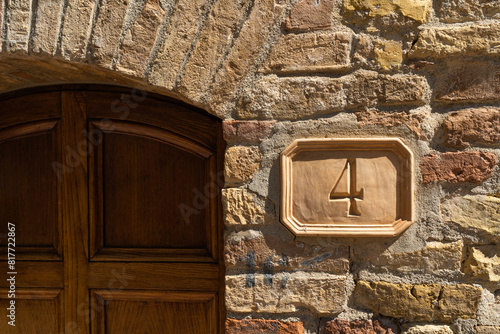 Wooden rectangle sign with the number four in classic brown font, hanging on brick facade of building.