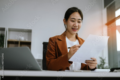 Business woman working at office with smartphone, laptop and documents on desk, financial adviser analyzing data.