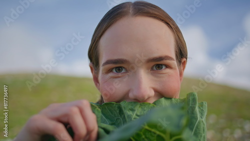 Woman holding lettuce leaf in front of face closeup. Smiling lady examining kale photo