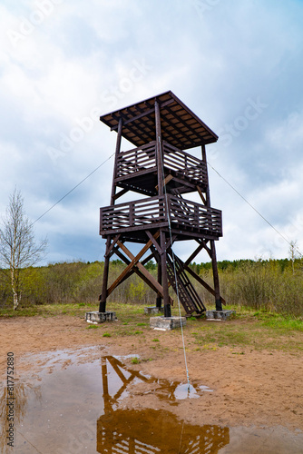 Beautiful image of a birdwatching tower reflecting in a puddle, set against a backdrop of cloudy skies and greenery. Perfect for nature and wildlife observation themes.