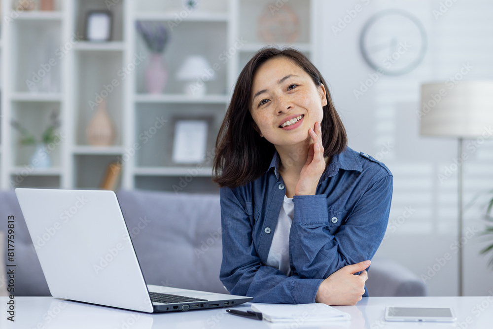Smiling woman working from home office with laptop, notepad, and mobile device. Cozy home interior in the background. Smiling woman working from home office with laptop, notepad, and mobile device. Cozy home interior in the background.
