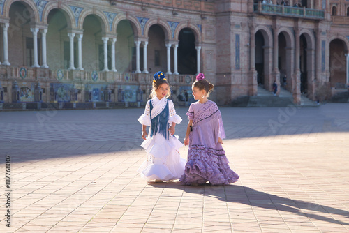 Two girls dancing flamenco walking and talking happily, with typical flamenco dress in a nice square in Seville. Dance concept, flamenco, typical Spanish, Seville, Spain.