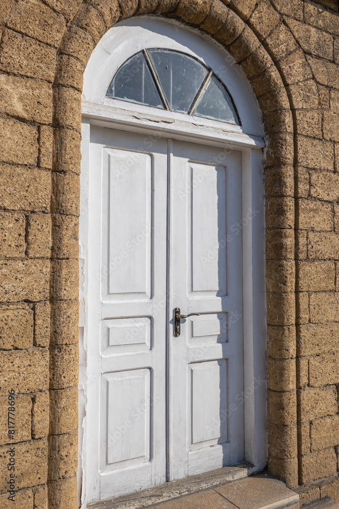 Fototapeta premium The vaulted entrance to the house. White wooden door. The masonry walls of the house are made of natural stone. Environmentally friendly building material. The shell rock.