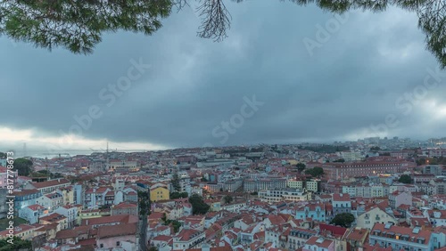 Panorama showing aerial cityscape day to night transition from Miradouro da Graca viewpoint in Lisbon city after sunset. Dramatic clouds over historic houses with red roofs and evening illumination photo