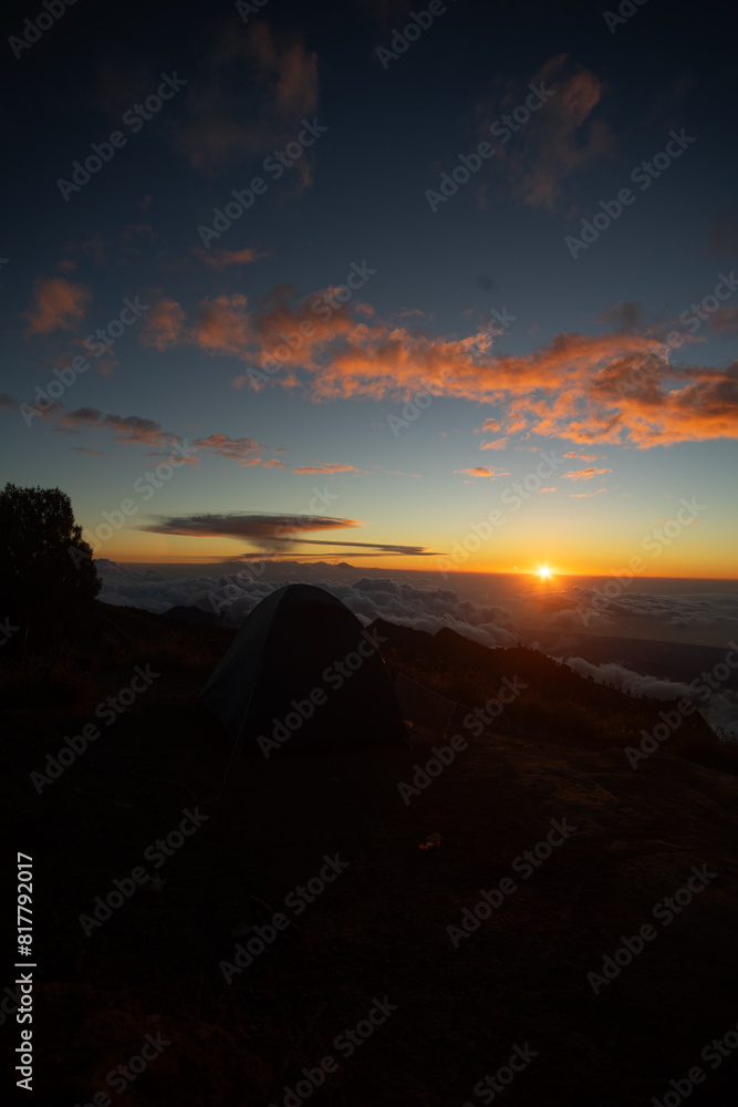 A serene sunset above the clouds with a tent silhouetted against the vibrant sky. A serene sunset above the clouds with a tent silhouetted against the vibrant sky.