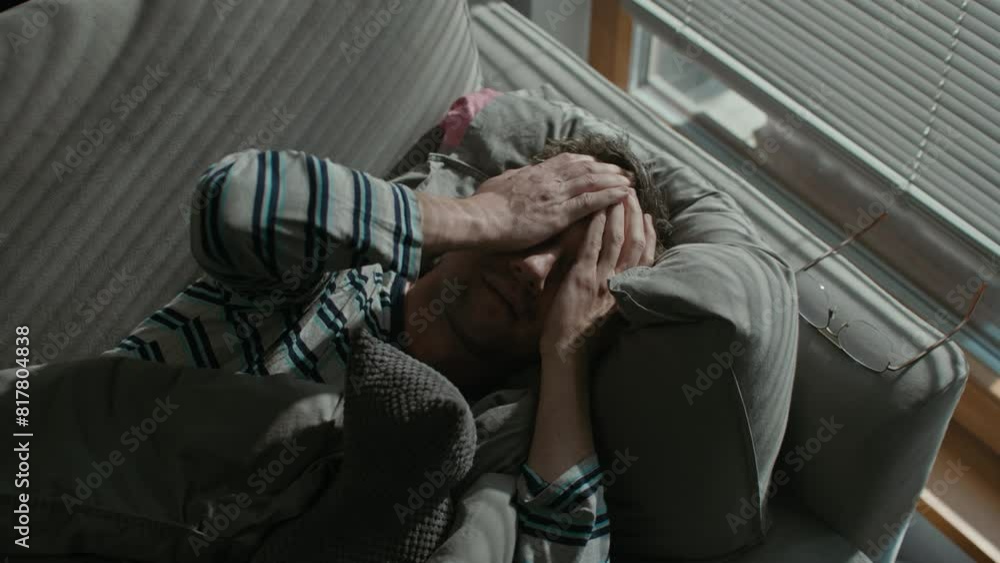 A depressed middle-aged man lies on the sofa in his flat in the morning A depressed middle-aged man lies on the sofa in his flat in the morning