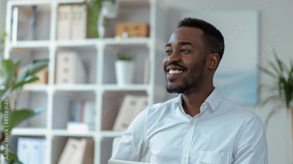 smiling African man in white shirt sits in modern office with shelves and plants in the background. He appears happy relaxed, looking away from camera, suggesting positive, professional environment smiling African man in white shirt sits in modern office with shelves and plants in the background. He appears happy relaxed, looking away from camera, suggesting positive, professional environment