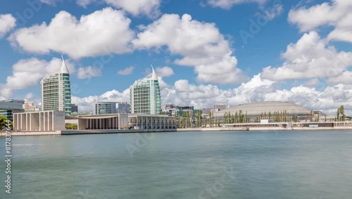 Panorama showing Parque das Nacoes or Park of Nations district timelapse in Lisbon, Portugal. Telecabine cable cars overlook Vasco da Gama bridge on Tagus river. Modern buildings reflected in water photo