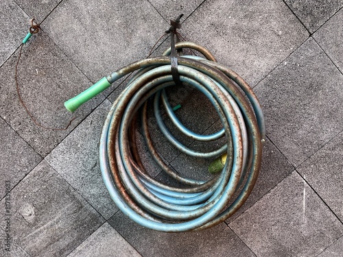 Photography Dirty blue watering hose with sprinkler hanged on the wall outside a house