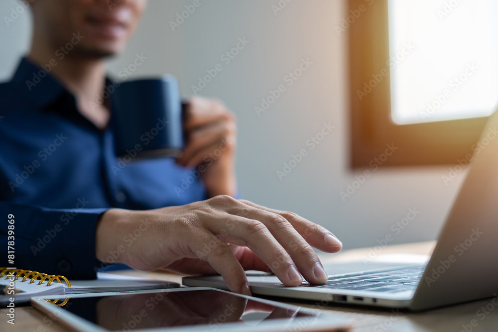 A man is typing on a laptop while holding a cup of coffee. Concept of productivity and focus, as the man is working on his computer while enjoying a hot