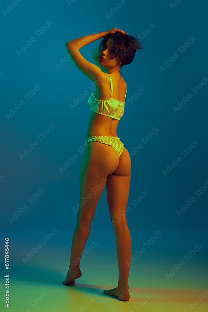 Full-length image of sensual, beautiful young girl with slim body shape posing in elegant white lingerie against cyan background in neon. Concept of natural beauty, skin care, sport, wellness, health Full-length image of sensual, beautiful young girl with slim body shape posing in elegant white lingerie against cyan background in neon. Concept of natural beauty, skin care, sport, wellness, health