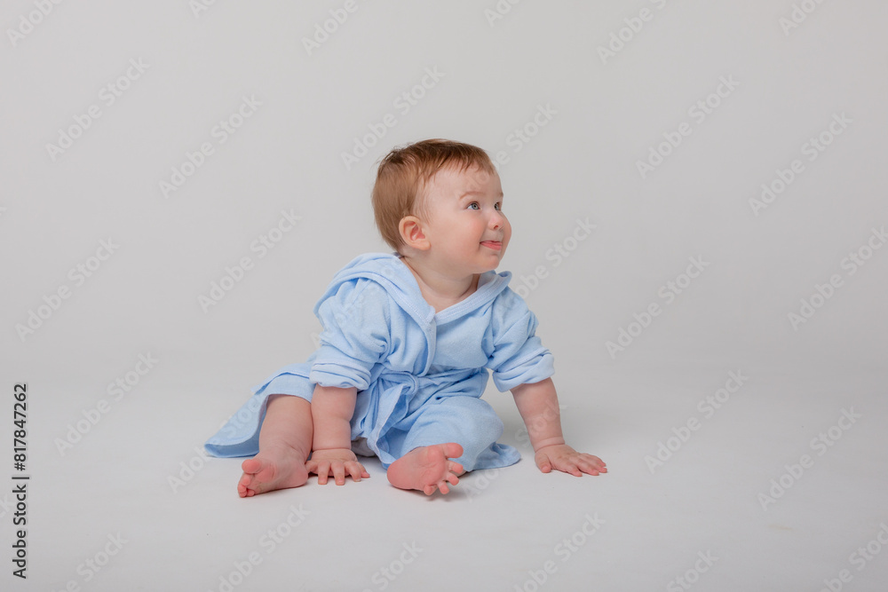 Cute happy laughing baby in a soft bathrobe after bathing plays on a white background. The child is wrapped in a clean and dry towel. Washing, baby hygiene, health and skin care Cute happy laughing baby in a soft bathrobe after bathing plays on a white background. The child is wrapped in a clean and dry towel. Washing, baby hygiene, health and skin care