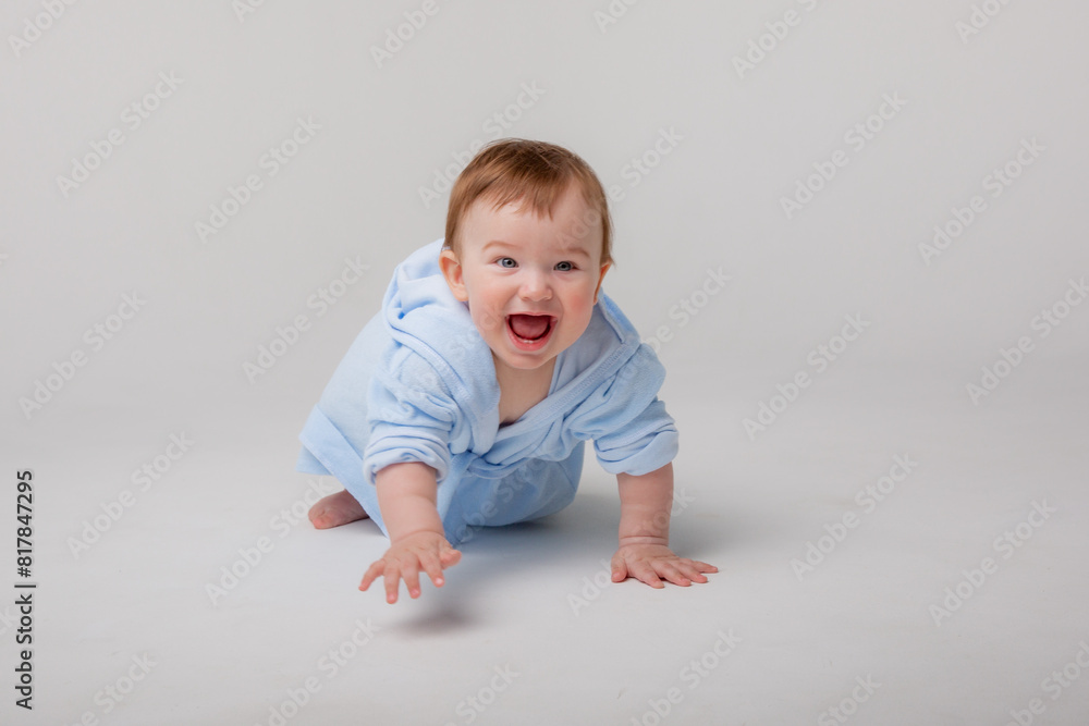 A cute happy laughing baby in a soft bathrobe crawls on a white background after bathing. The child is wrapped in a clean and dry towel. Washing, baby hygiene, health and skin care A cute happy laughing baby in a soft bathrobe crawls on a white background after bathing. The child is wrapped in a clean and dry towel. Washing, baby hygiene, health and skin care