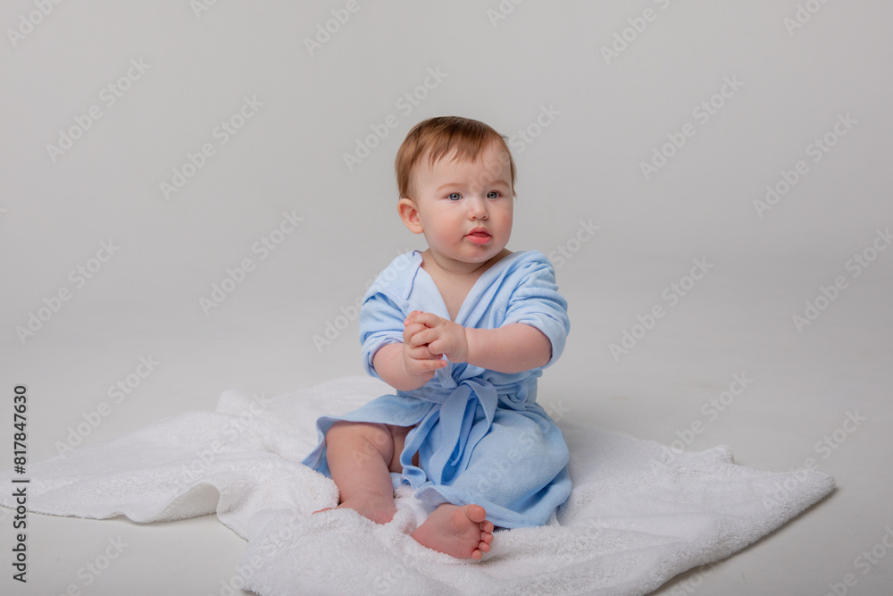 Cute happy laughing baby in a soft bathrobe after bathing plays on a white background. The child is wrapped in a clean and dry towel. Washing, baby hygiene, health and skin care Cute happy laughing baby in a soft bathrobe after bathing plays on a white background. The child is wrapped in a clean and dry towel. Washing, baby hygiene, health and skin care