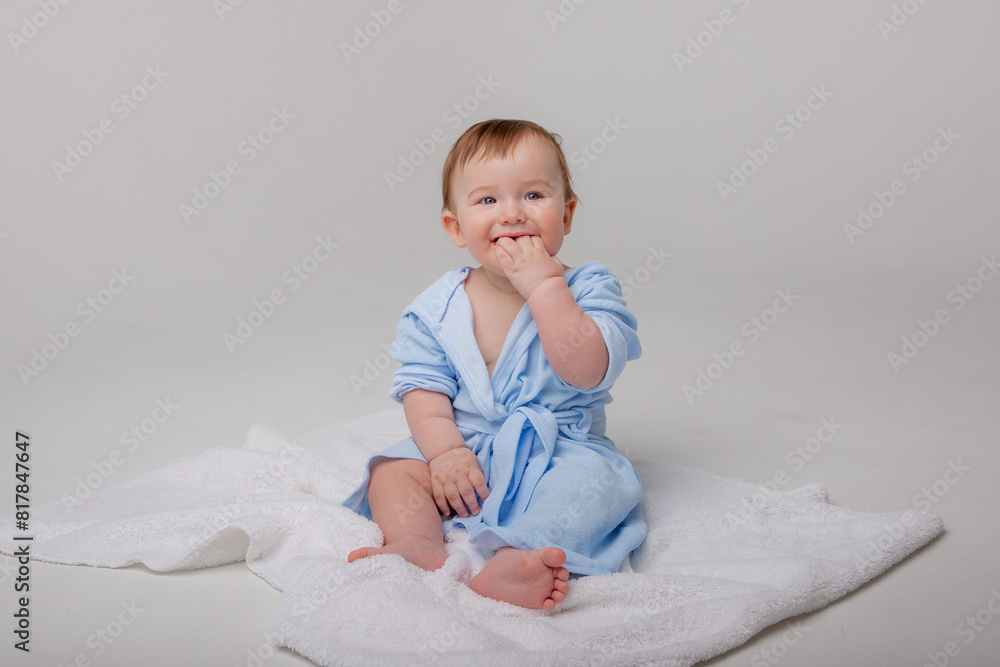 Cute happy laughing baby in a soft bathrobe after bathing plays on a white background. The child is wrapped in a clean and dry towel. Washing, baby hygiene, health and skin care
