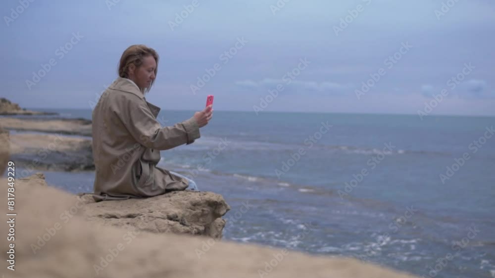 A woman with a mobile phone is talking on a video call on a cliff by the sea. Spain, Alicante A woman with a mobile phone is talking on a video call on a cliff by the sea. Spain, Alicante
