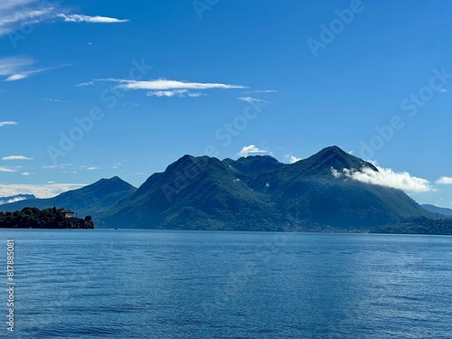 Captivating view of lush green mountains and a small island Isola Madre on Lake Maggiore under a clear blue sky in Verbano-Cusio-Ossola, Piedmont, Italy