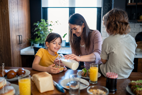 Little girl pouring milk into cornflakes cereals with mothers help. Daughter and mother preparing morning meal together. Cheerful family moments  bonding and quality time.