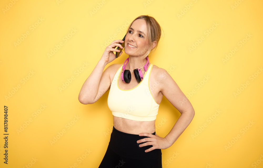 Young athletic woman using mobile phone, standing against yellow background Young athletic woman using mobile phone, standing against yellow background