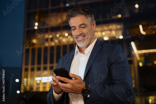 European latin middle age male entrepreneur businessman working on mobile cell phone. Confident mature hispanic senior business man holding smartphone cellphone  using app at busy street at evening