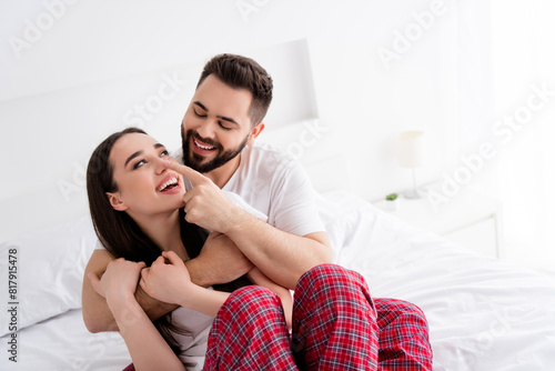 Photo of carefree positive couple wear white t-shirts touching nose embracing indoors apartment bedroom