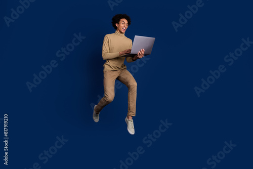 Full size photo of nice young man hold netbook running wear trendy beige outfit isolated on dark blue color background