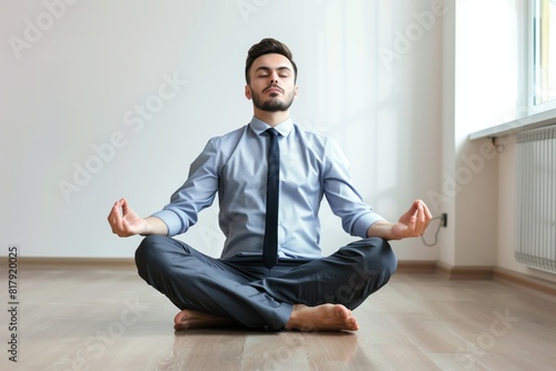 Businessman meditating in a lotus position on the floor of a minimalist office space. He is focusing on mindfulness and stress relief.
