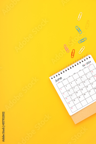 June 2024 desk calendar and paper clips on yellow color background.