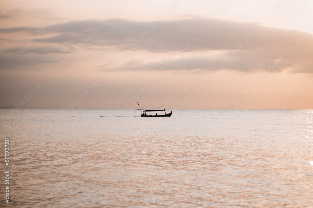 A fishing boat in the middle of the sea with a sunset background