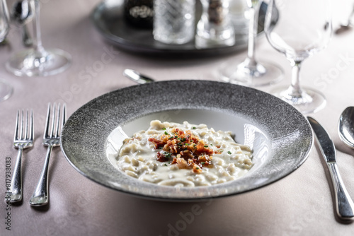 Halusky as traditional Slovak potato gnocchi with sheep cheese bryndza, fried bacon and chives served in a modern plate and on a festively laid restaurant table.