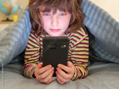 Young child looking at cellphone or mobile phone screen  alone in her bedroom
