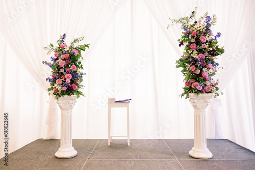 Two pillars with a beautiful floral arrangement set up on a stage, ready for a a wedding ceremony