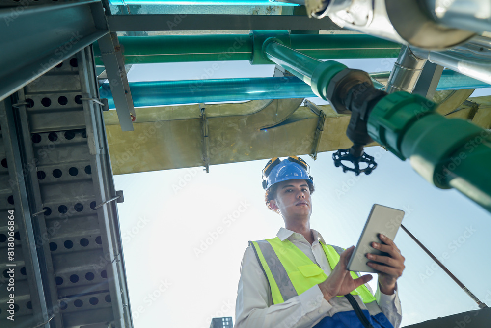 Male engineer monitoring machinery on a rooftop with city skyline in the background, wearing safety gear Male engineer monitoring machinery on a rooftop with city skyline in the background, wearing safety gear