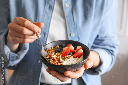 Woman eating tasty granola with berries, yogurt and seeds, closeup
