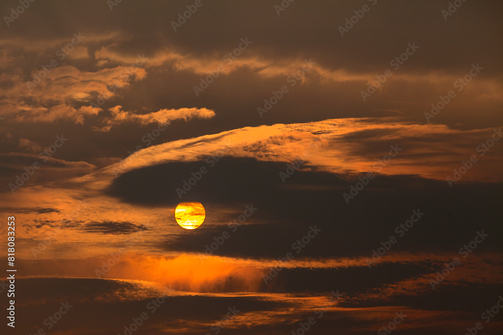 A mesmerizing sunset captured through dense, dramatic clouds. The sun, partially obscured by the clouds A mesmerizing sunset captured through dense, dramatic clouds. The sun, partially obscured by the clouds