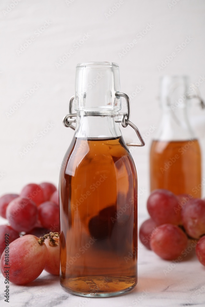 Wine vinegar in glass bottles and grapes on white marble table Wine vinegar in glass bottles and grapes on white marble table