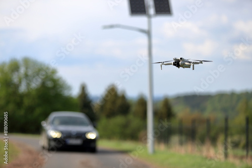Dron w locie, w powietrzu, w tle panele słoneczne z latarnią uliczną, samochody osobowe na drodze.