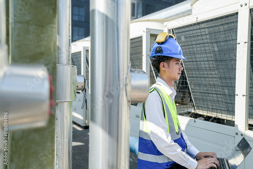 Industrial engineer adjusting pipeline valve with radio communication on construction site. Engineer on urban construction site using radio to coordinate with team on a sunny industrial rooftop.