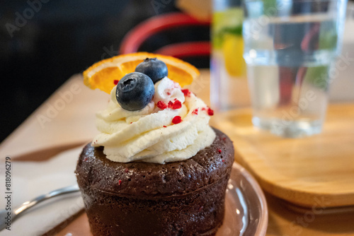Chocolate cupcake with whipped cream, blueberry and orange slice, on background glass of water