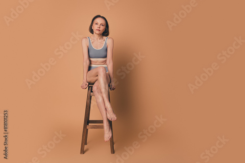 No retouch photo of charming lovely woman sitting stool empty space isolated on beige color background