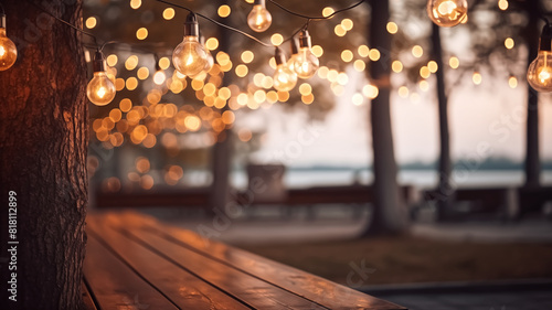 String lights hanging on a tree at an outdoor venue during sunset. Bokeh effect with warm lights. Evening and celebration concept. Design for banner, greeting card, invitation, postcard, poster.